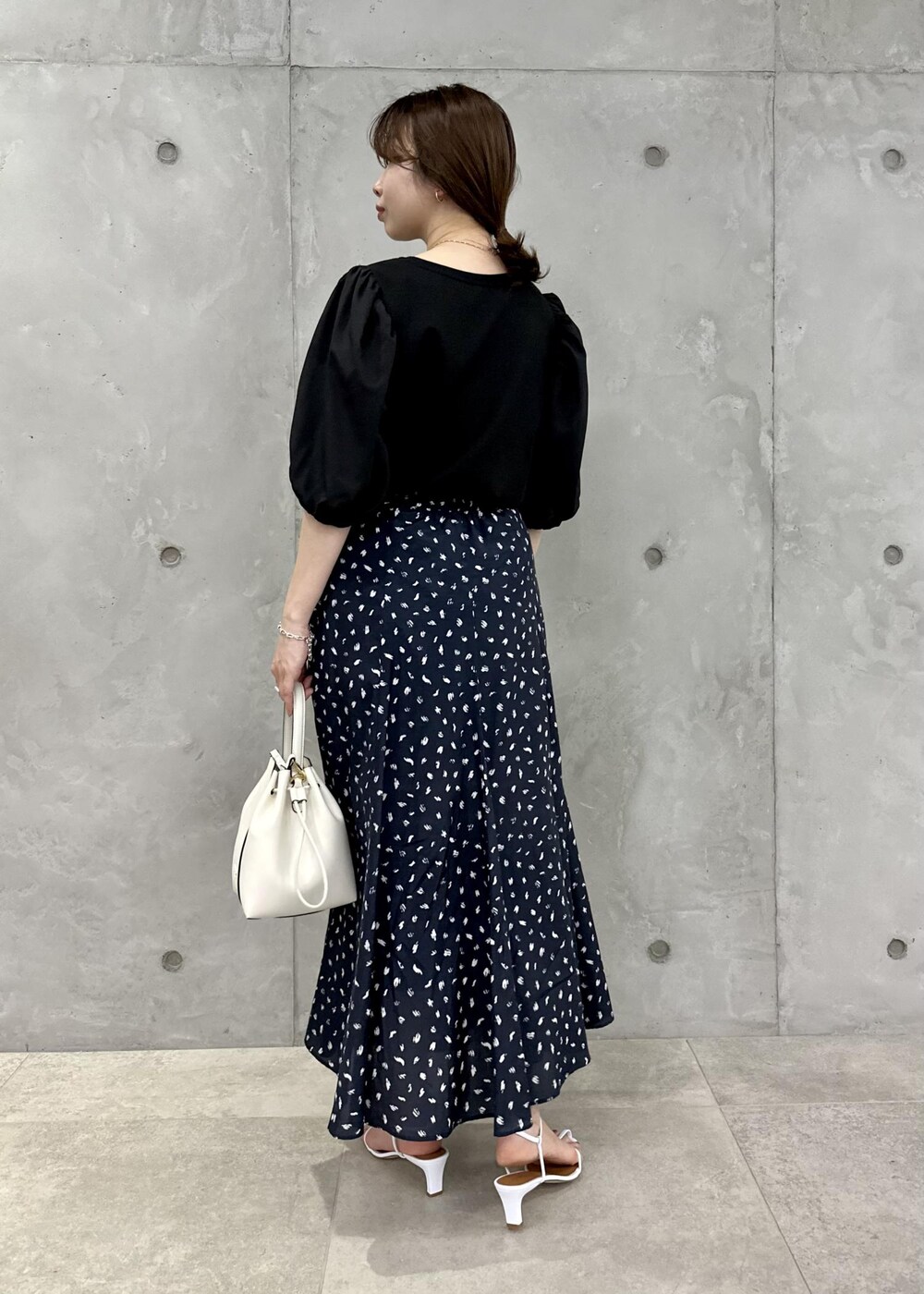 ブラック系のスカート、ホワイト系のハンドバッグ、ホワイト系のサンダルを着用したレディースの春コーディネートの3枚目の写真
