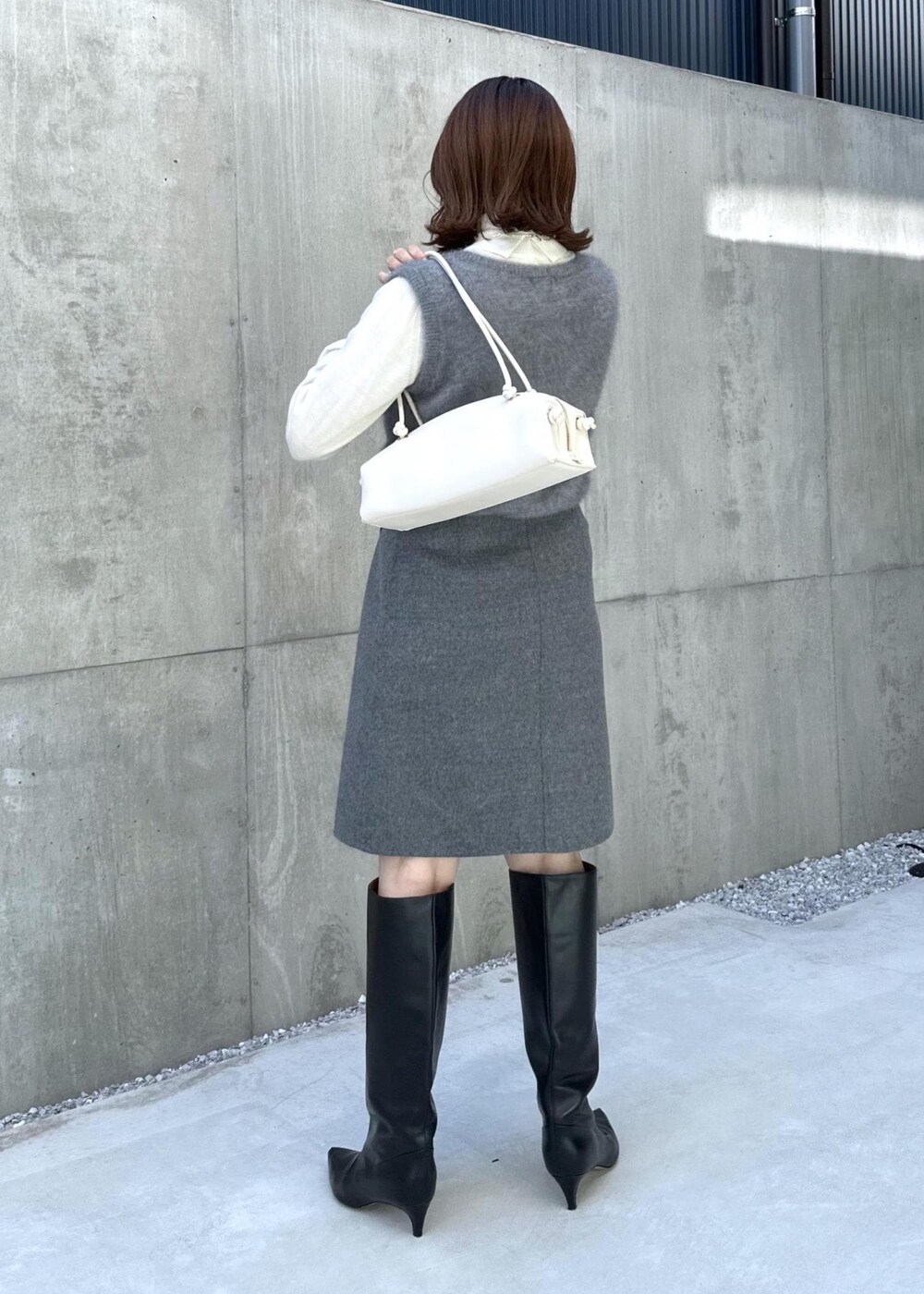 ブラック系のブーツ、ホワイト系のハンドバッグ、グレー系のベストを着用したレディースの秋コーディネートの8枚目の写真