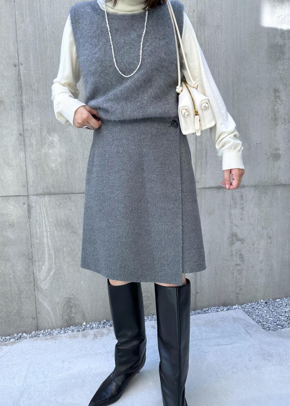 ブラック系のブーツ、ホワイト系のハンドバッグ、グレー系のベストを着用したレディースの秋コーディネートの6枚目の写真
