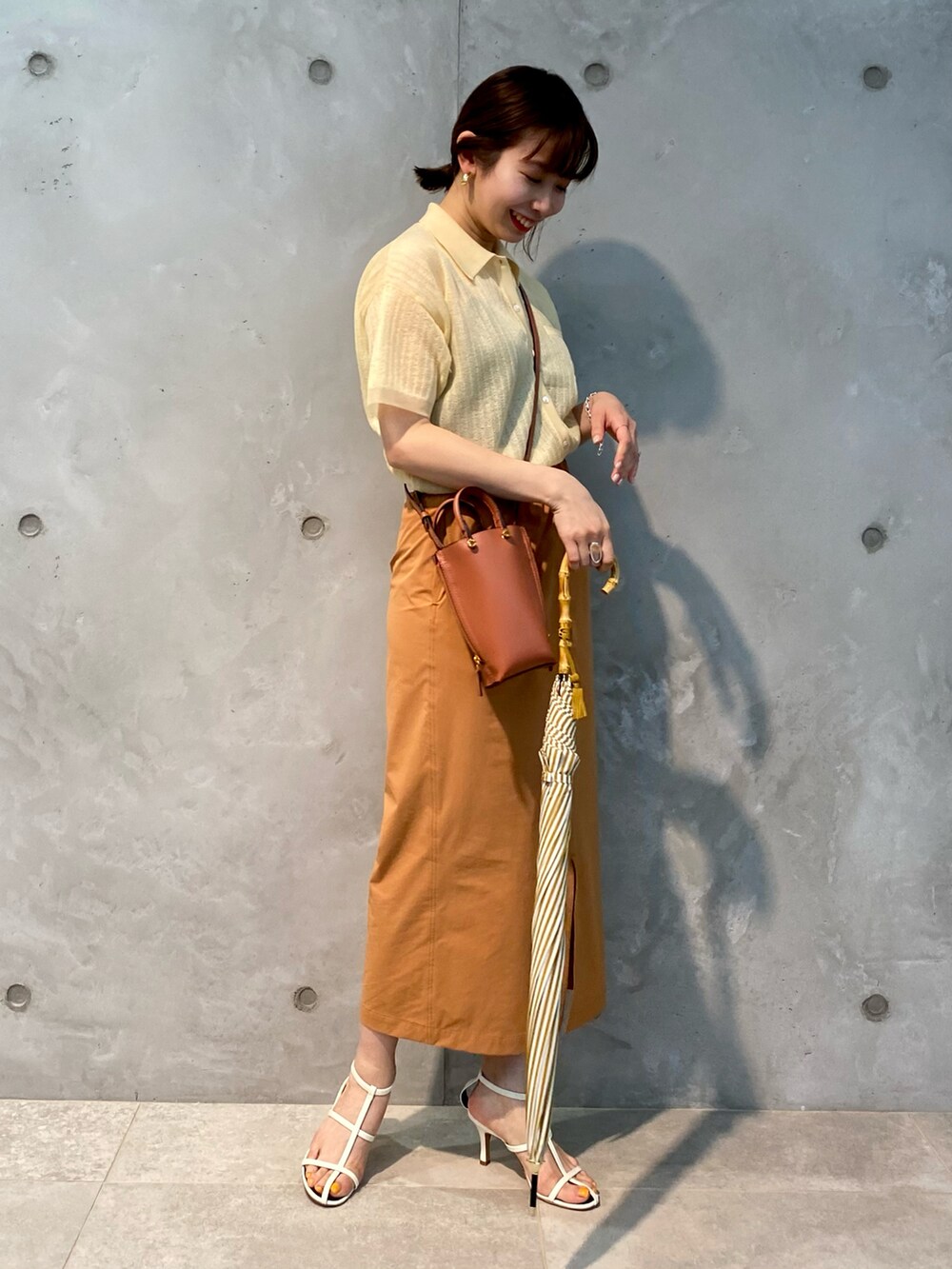 ベージュ系のニット/セーター、オレンジ系のスカート、ブラウン系のショルダーバッグを着用したレディースの春コーディネートの2枚目の写真