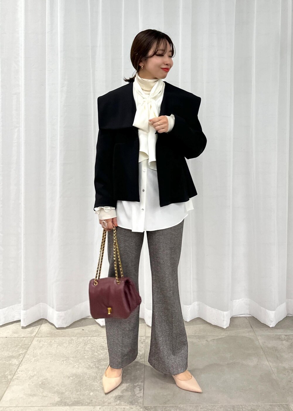 レッド系のハンドバッグ、ベージュ系のパンプス、グレー系のその他パンツを着用したレディースの秋コーディネートの2枚目の写真