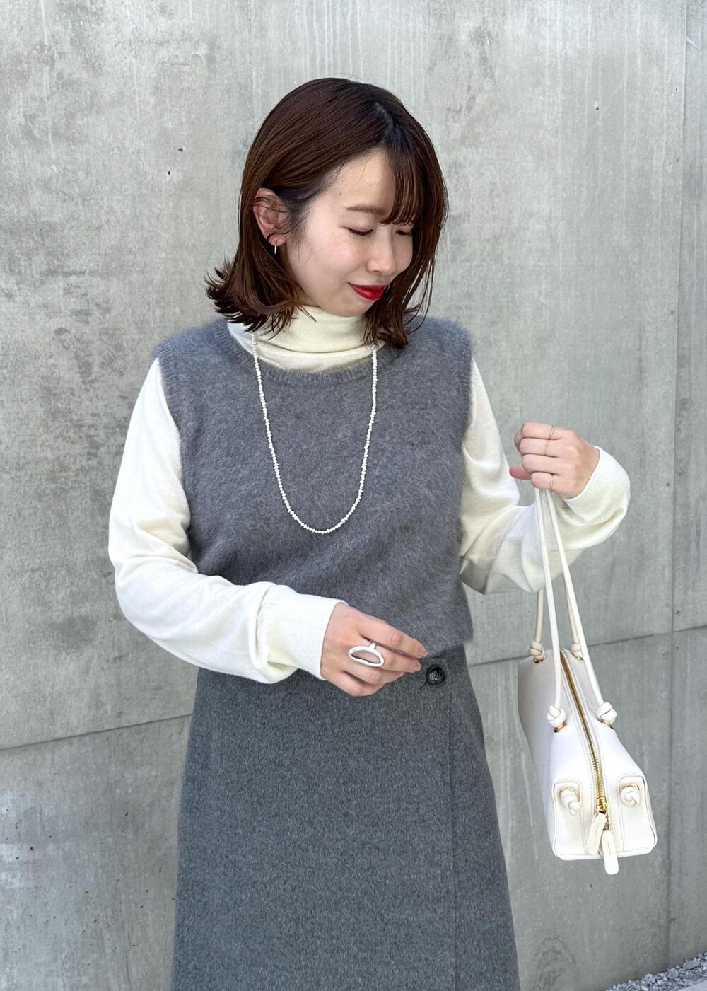 ブラック系のブーツ、ホワイト系のハンドバッグ、グレー系のベストを着用したレディースの秋コーディネートの4枚目の写真