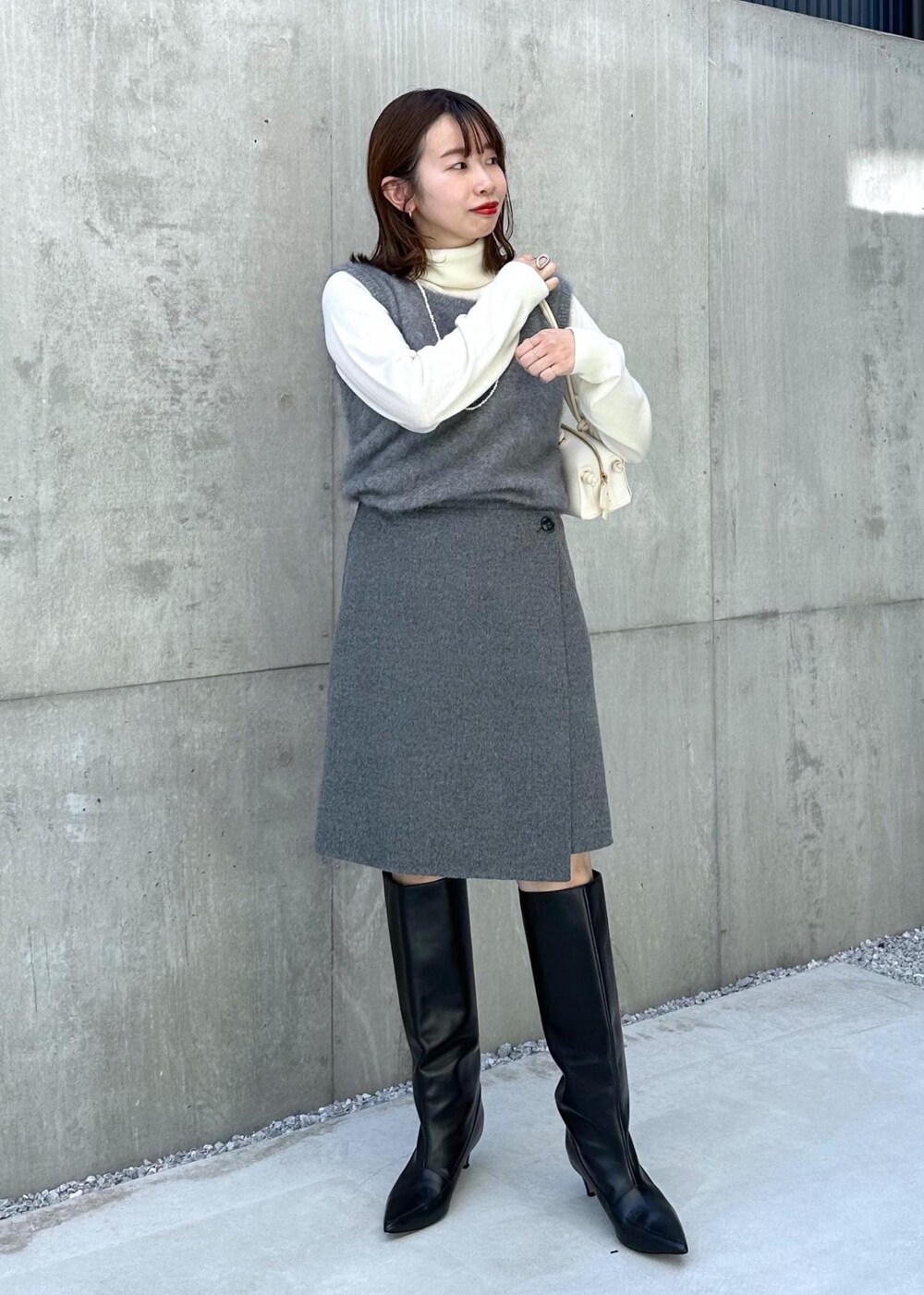 ブラック系のブーツ、ホワイト系のハンドバッグ、グレー系のベストを着用したレディースの秋コーディネートの9枚目の写真