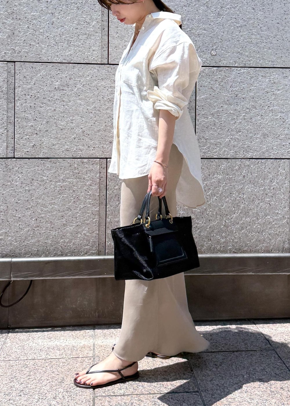 ブラック系のハンドバッグ、ベージュ系のスカート、ホワイト系のシャツ/ブラウスを着用したレディースの夏コーディネートの3枚目の写真