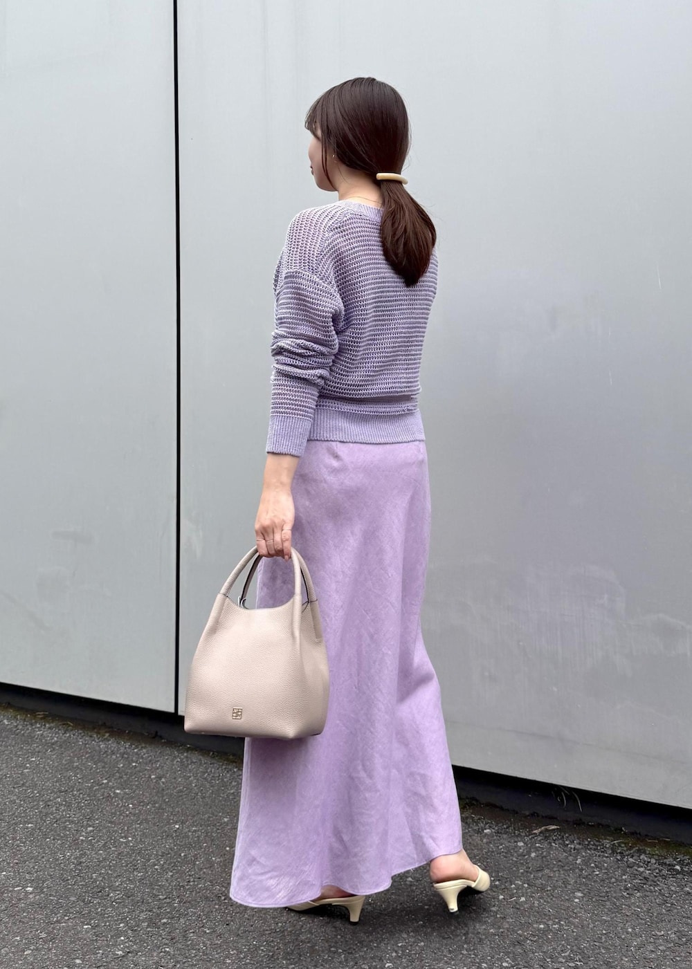 パープル系のニット/セーター、パープル系のスカート、グレー系のハンドバッグを着用したレディースの春コーディネートの3枚目の写真