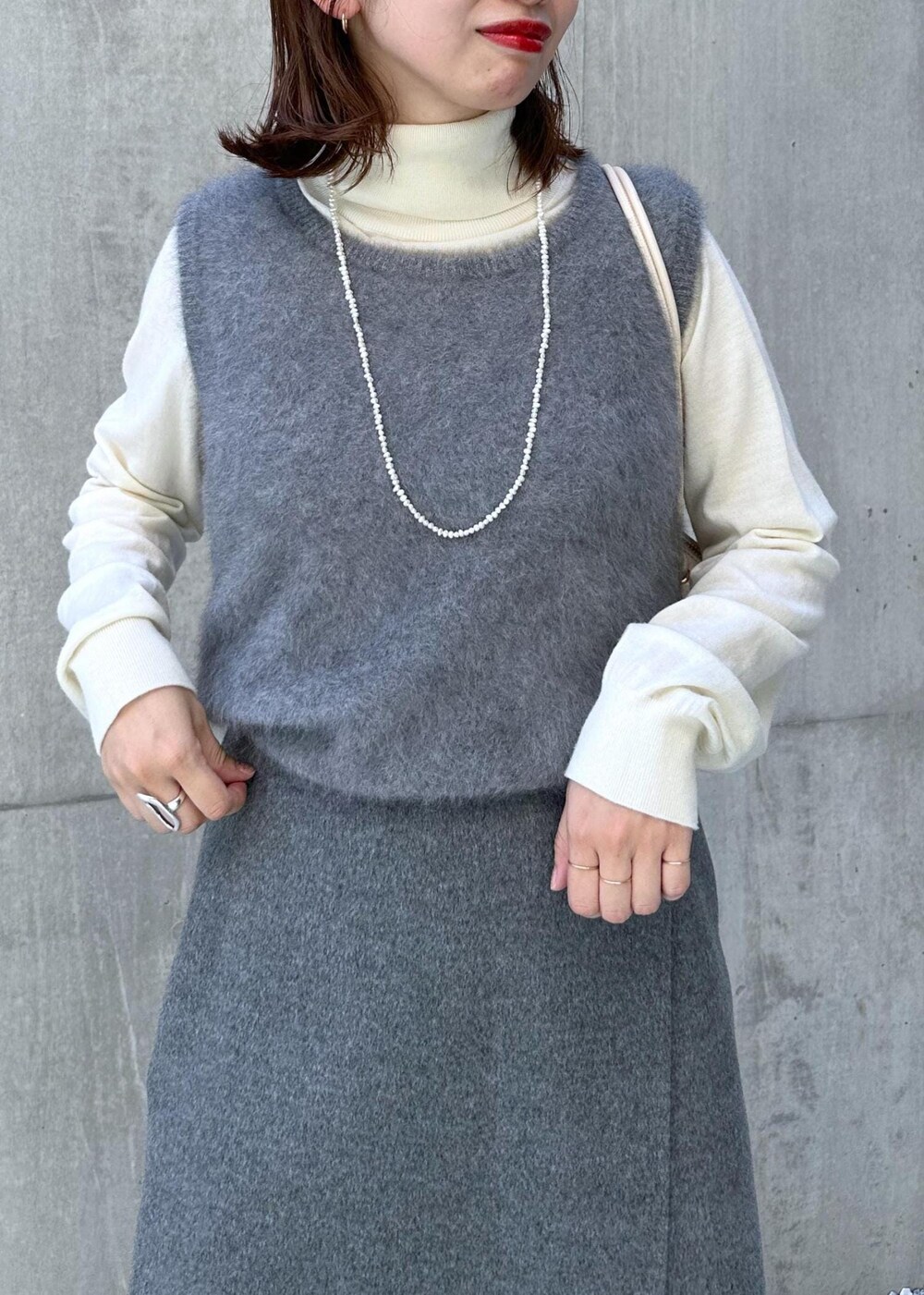 ブラック系のブーツ、ホワイト系のハンドバッグ、グレー系のベストを着用したレディースの秋コーディネートの5枚目の写真