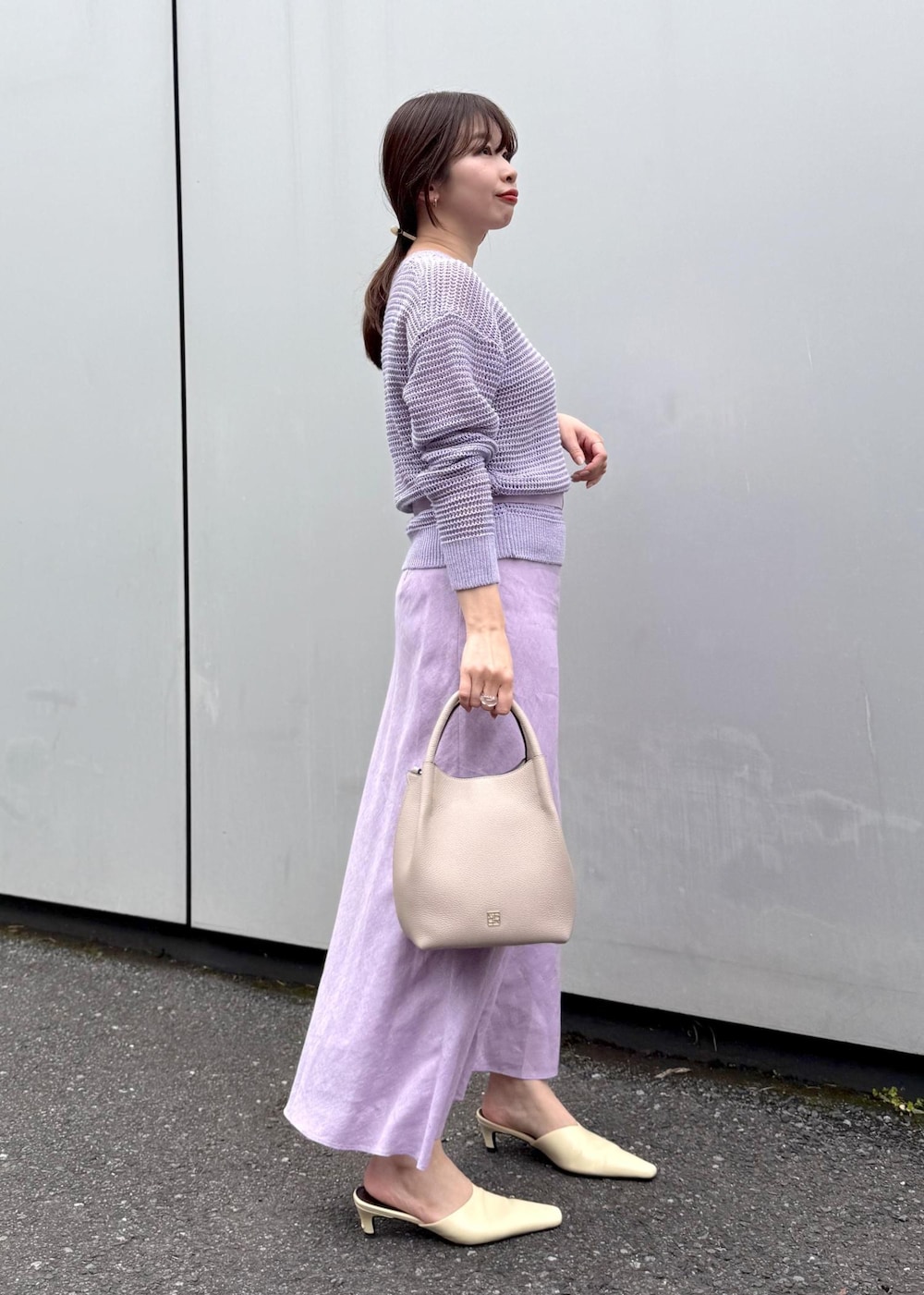 パープル系のニット/セーター、パープル系のスカート、グレー系のハンドバッグを着用したレディースの春コーディネートの2枚目の写真
