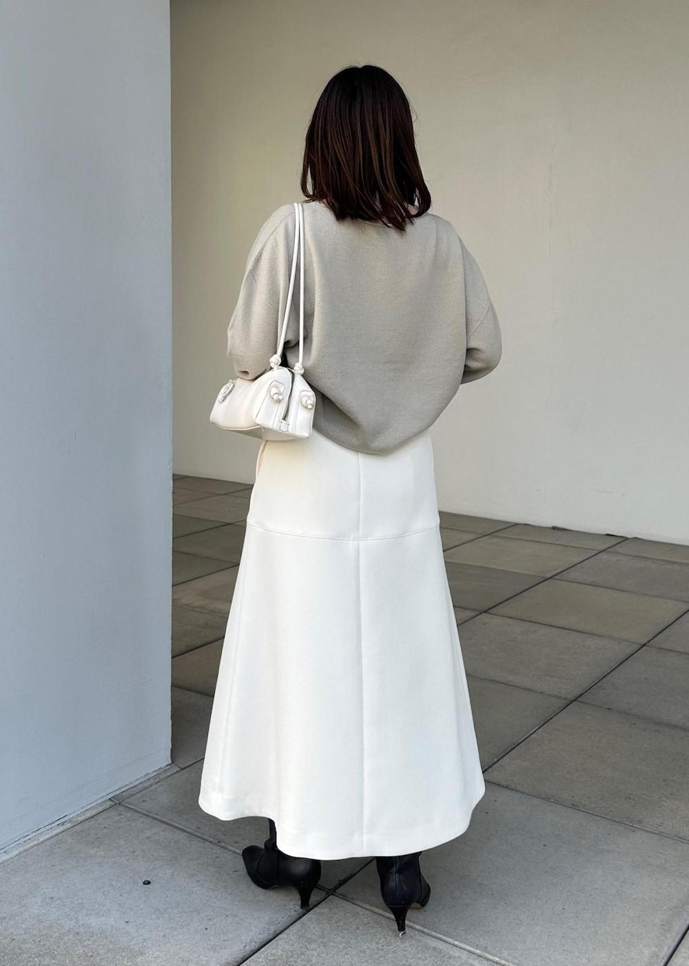 ホワイト系のハンドバッグ、ホワイト系のスカート、ベージュ系のニット/セーターを着用したレディースの冬コーディネートの3枚目の写真