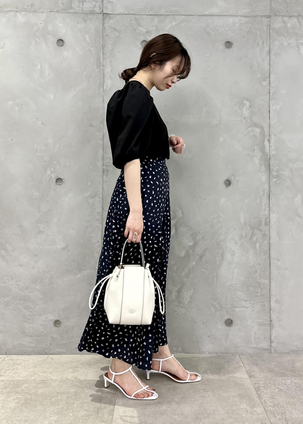 ブラック系のスカート、ホワイト系のハンドバッグ、ホワイト系のサンダルを着用したレディースの春コーディネートの2枚目の写真