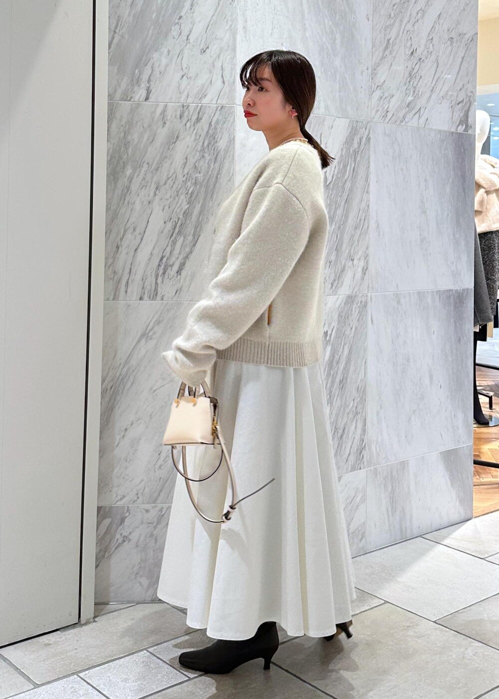 ベージュ系のショルダーバッグ、ホワイト系のカーディガン/ボレロ、ホワイト系のスカートを着用したレディースの冬コーディネートの2枚目の写真