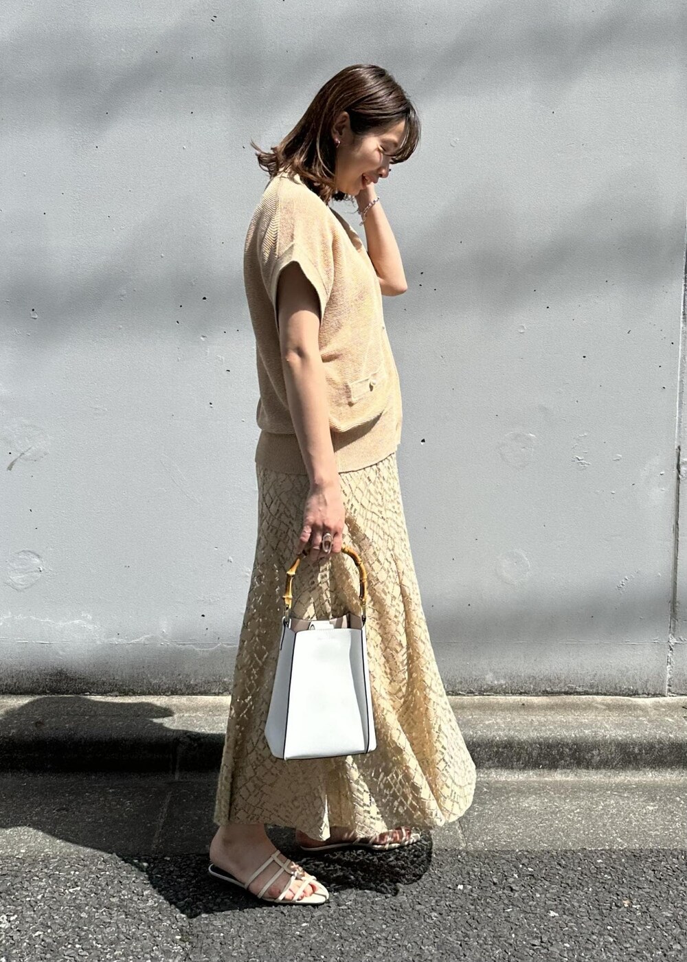 ベージュ系のスカート、ホワイト系のハンドバッグ、ホワイト系のサンダルを着用したレディースの春コーディネートの2枚目の写真