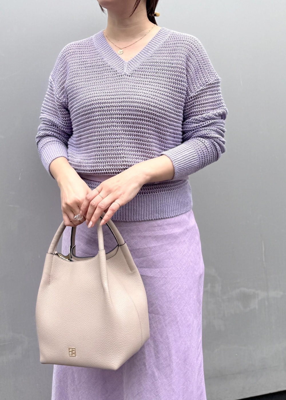 パープル系のニット/セーター、パープル系のスカート、グレー系のハンドバッグを着用したレディースの春コーディネートの4枚目の写真