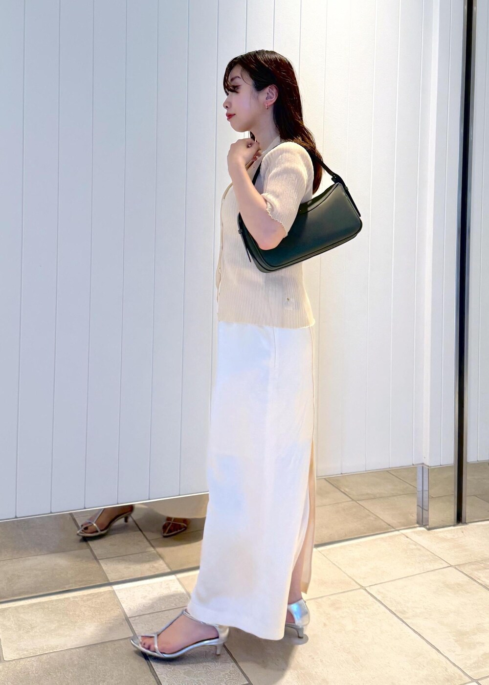 ホワイト系のスカート、ベージュ系のニット/セーター、グリーン系のハンドバッグを着用したレディースの夏コーディネートの2枚目の写真