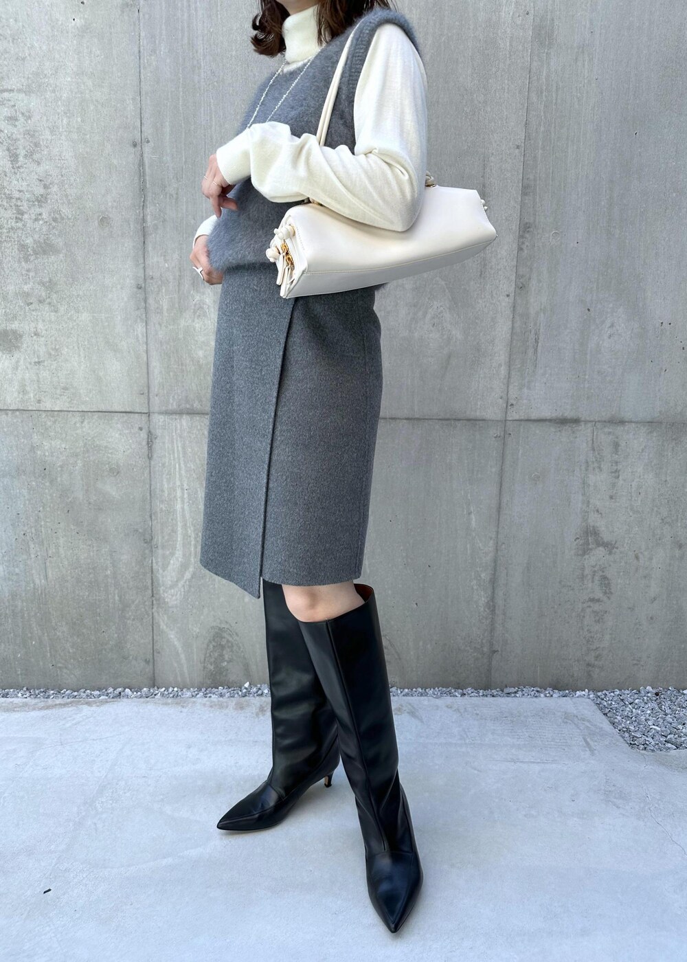 ブラック系のブーツ、ホワイト系のハンドバッグ、グレー系のベストを着用したレディースの秋コーディネートの7枚目の写真