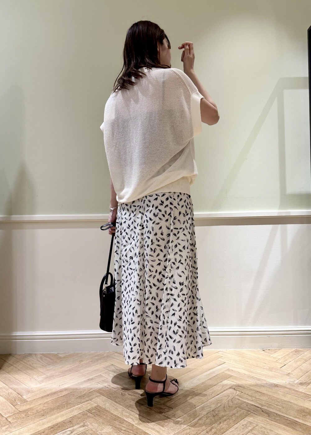 ブラック系のハンドバッグ、ホワイト系のスカート、ブラック系のサンダルを着用したレディースの夏コーディネートの2枚目の写真