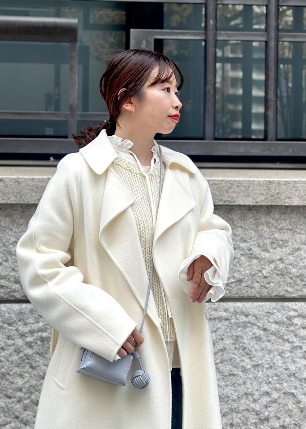 ブルー系のショルダーバッグ、ホワイト系のチェスターコート、ホワイト系のニット/セーターを着用したレディースの冬コーディネートの5枚目の写真