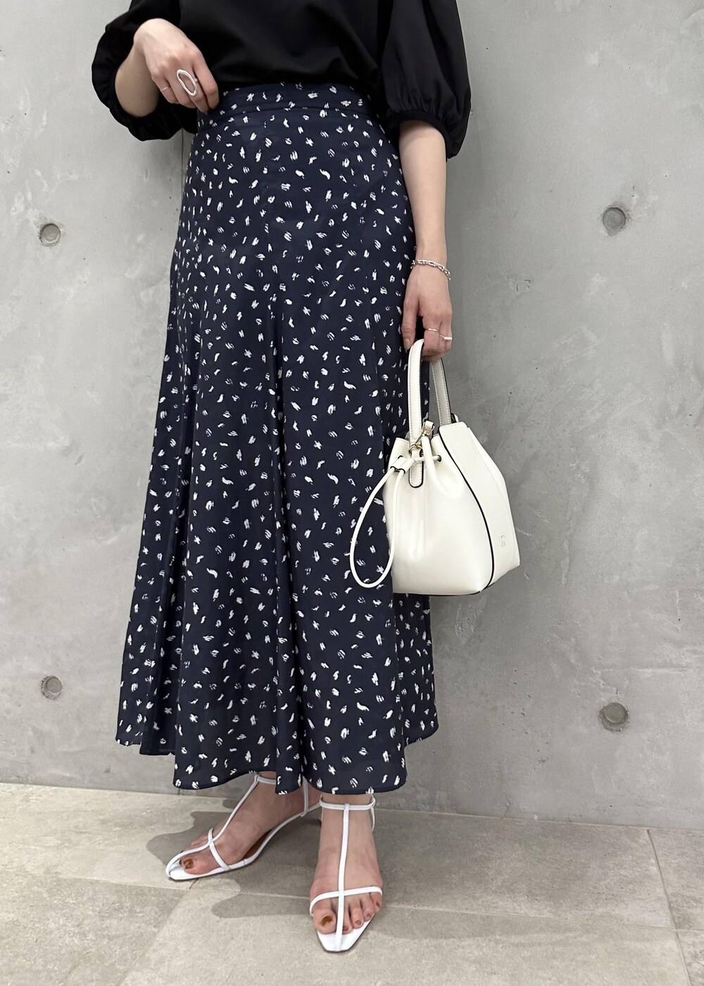 ブラック系のスカート、ホワイト系のハンドバッグ、ホワイト系のサンダルを着用したレディースの春コーディネートの6枚目の写真