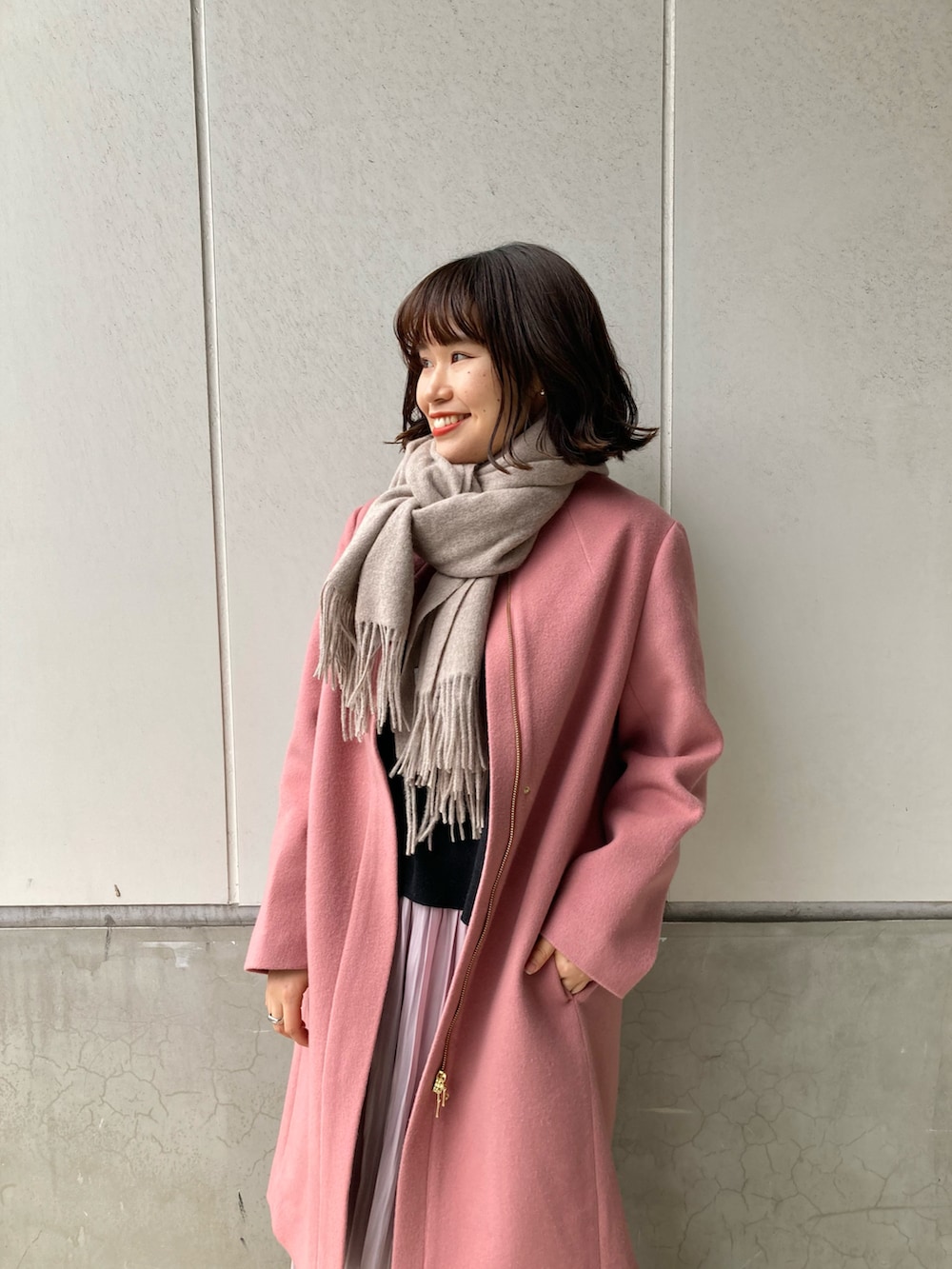 ピンク系のノーカラーコート、ピンク系のスカート、ベージュ系のブーツを着用したレディースの冬コーディネートの2枚目の写真