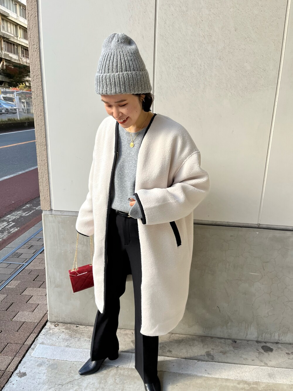 ホワイト系のノーカラーコート、グレー系のニット/セーター、レッド系のショルダーバッグを着用したレディースの冬コーディネートの2枚目の写真