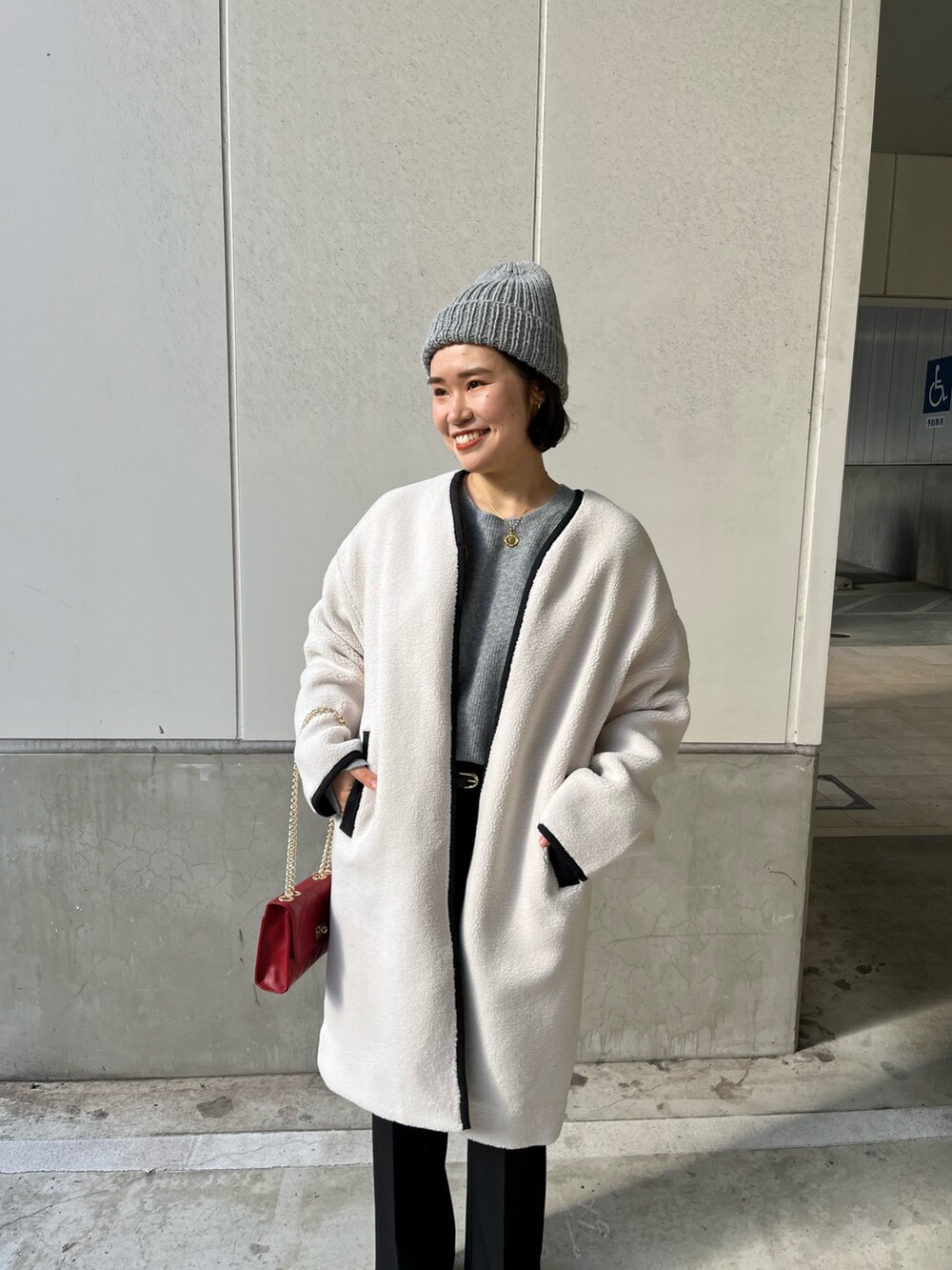 ホワイト系のノーカラーコート、グレー系のニット/セーター、レッド系のショルダーバッグを着用したレディースの冬コーディネートの3枚目の写真