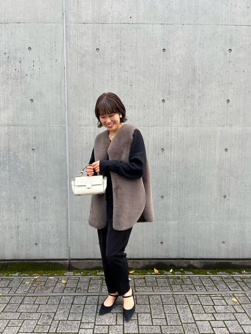 ブラウン系のベスト、ブラック系のその他パンツ、ホワイト系のショルダーバッグを着用したレディースの冬コーディネートの2枚目の写真