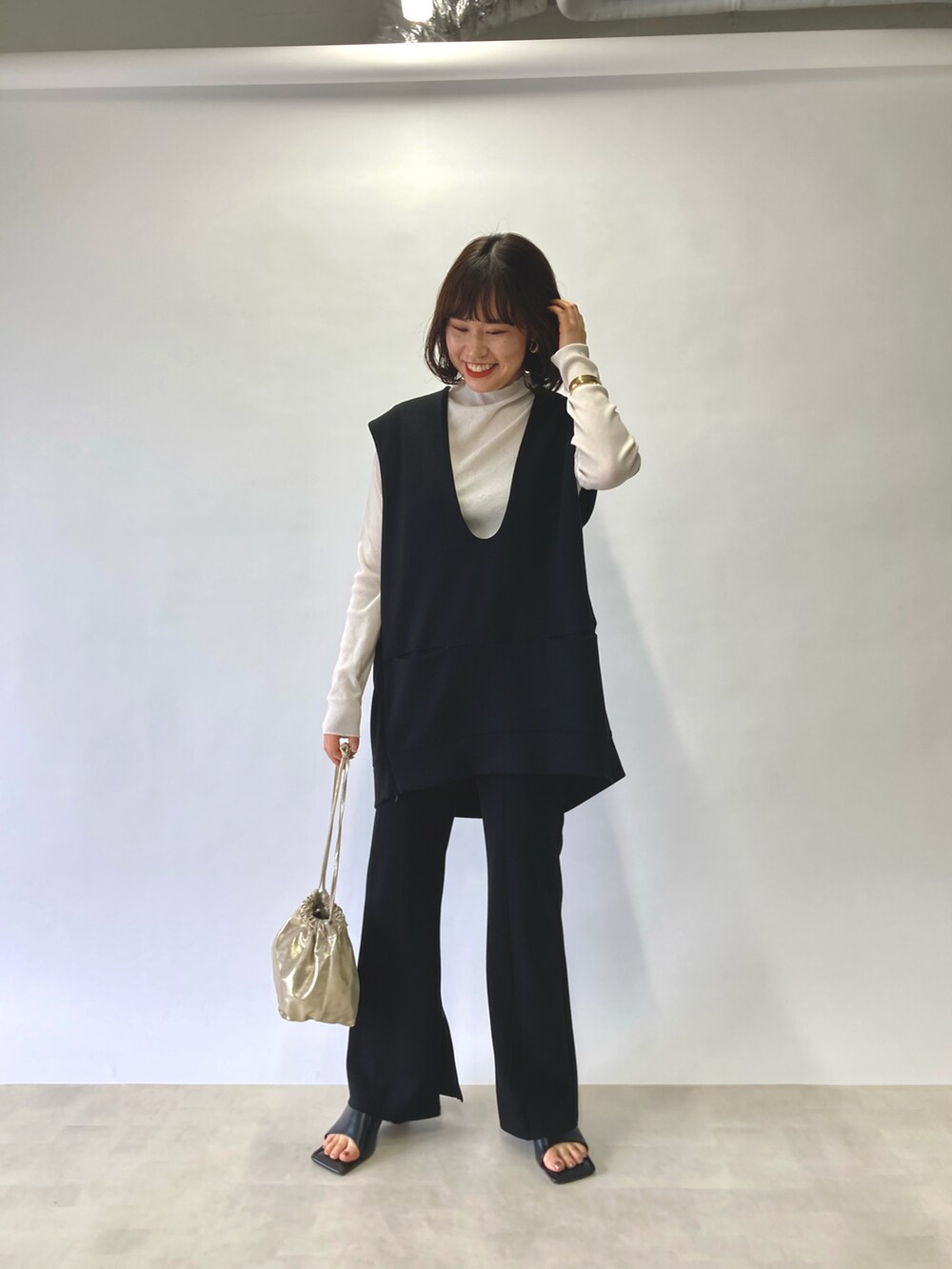 ブラック系のベスト、ホワイト系のTシャツ/カットソー、ゴールド系のショルダーバッグを着用したレディースの春コーディネートの2枚目の写真