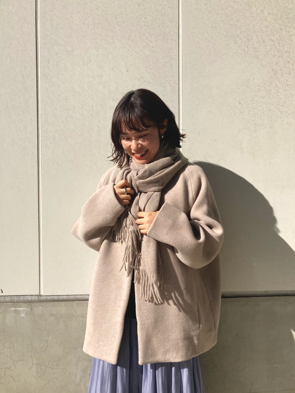 ベージュ系のノーカラーコート、ブルー系のスカート、ブラック系のブーツを着用したレディースの冬コーディネートの2枚目の写真