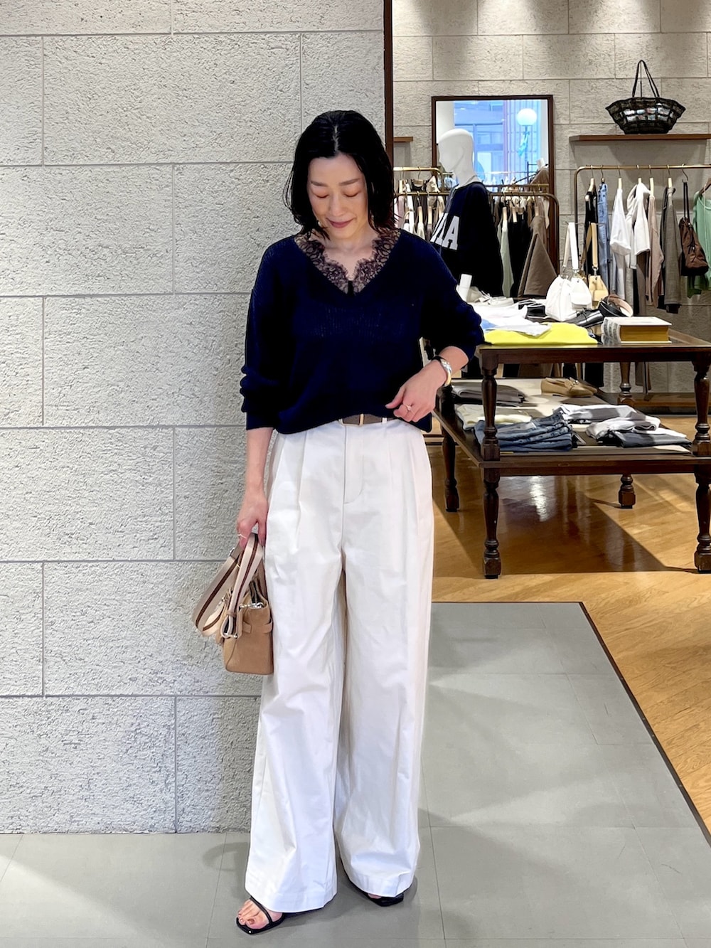 ホワイト系のチノパンツ、ベージュ系のトートバッグ、ブルー系のニット/セーターを着用したレディースの春コーディネートの2枚目の写真