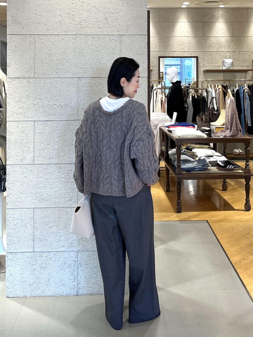 グレー系のスラックス、ブラック系のブーツ、ホワイト系のハンドバッグを着用したレディースの冬コーディネートの4枚目の写真