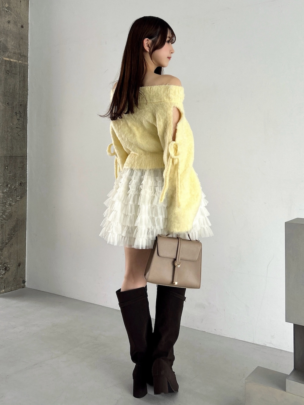 イエロー系のニット/セーター、ホワイト系のスカート、ブラウン系のブーツを着用したレディースの秋コーディネートの5枚目の写真