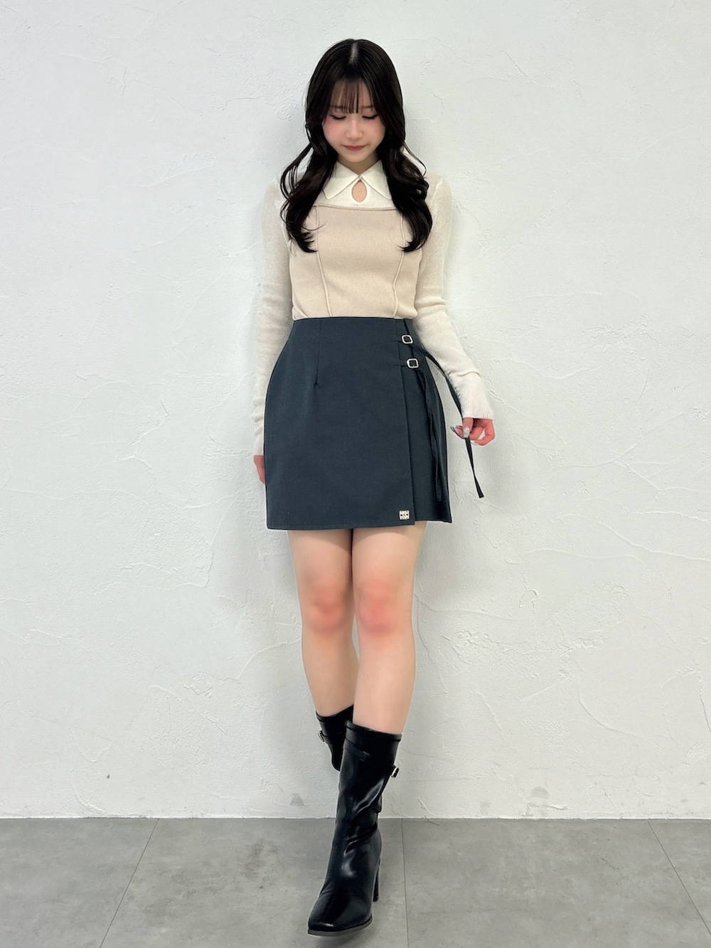 グレー系のスカート、ブラック系のブーツ、ベージュ系のニット/セーターを着用したレディースの春コーディネートの2枚目の写真