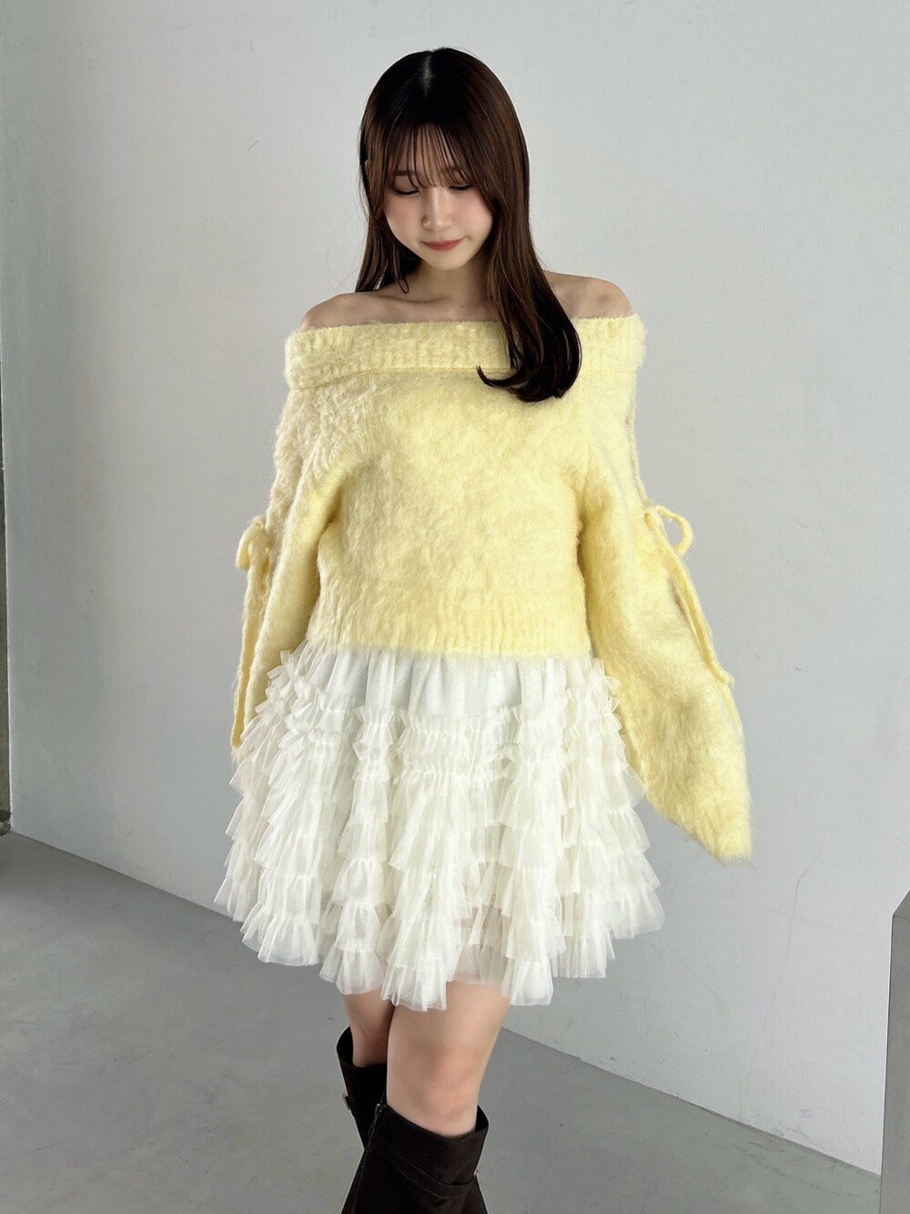 イエロー系のニット/セーター、ホワイト系のスカート、ブラウン系のブーツを着用したレディースの秋コーディネートの7枚目の写真