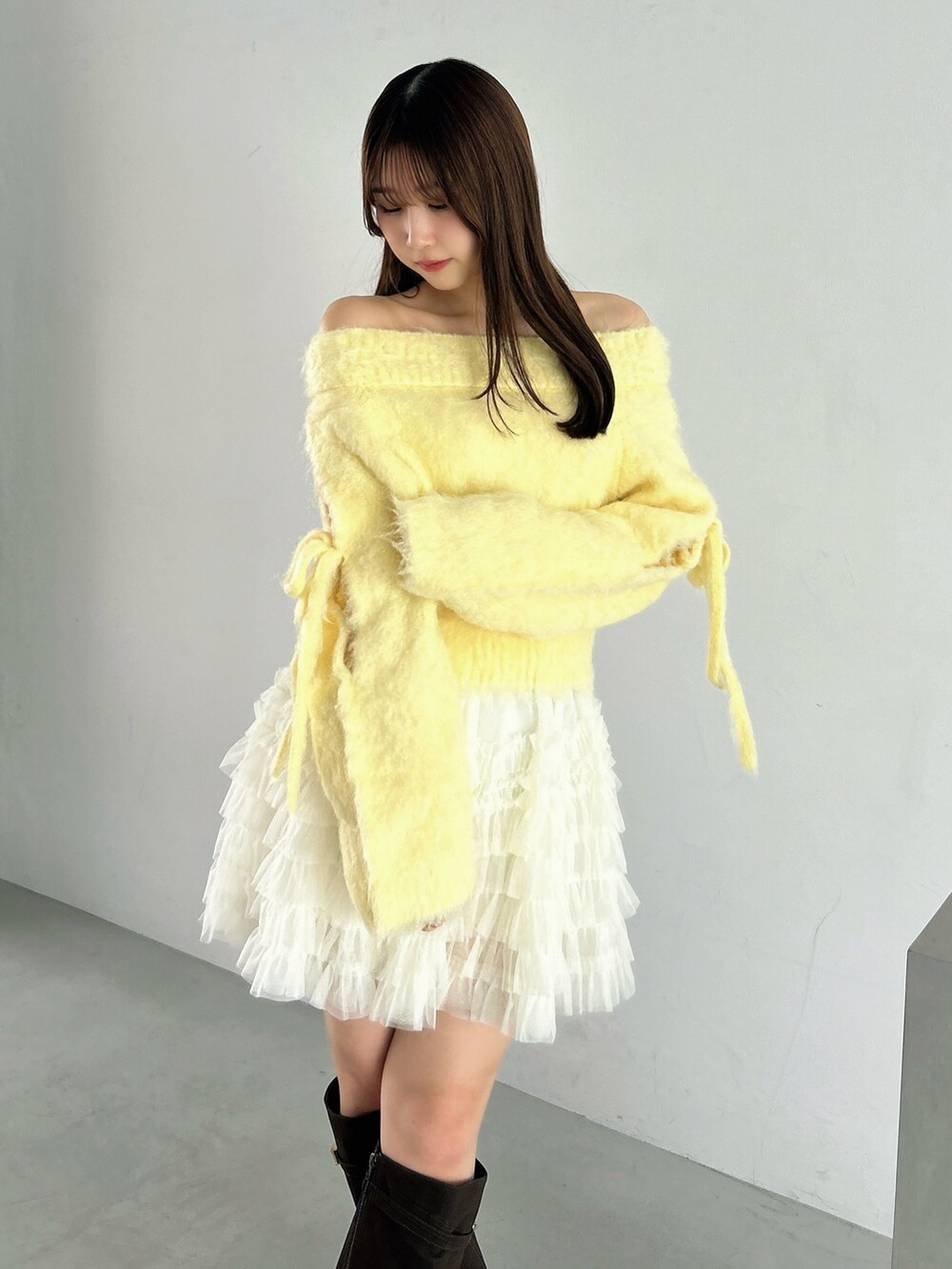 イエロー系のニット/セーター、ホワイト系のスカート、ブラウン系のブーツを着用したレディースの秋コーディネートの8枚目の写真