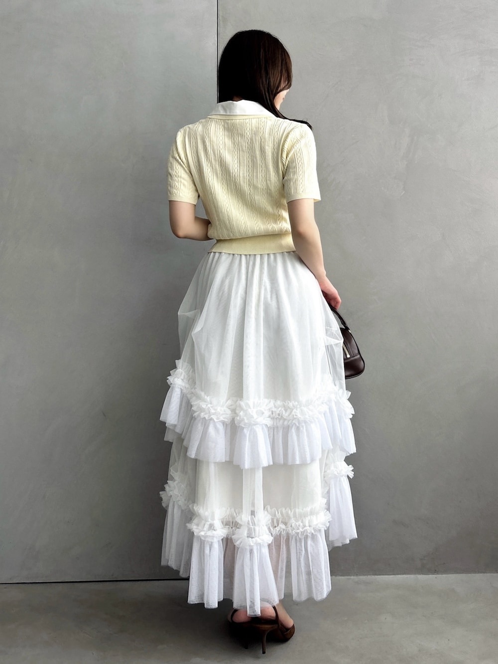 イエロー系のニット/セーター、ホワイト系のスカート、ブラウン系のハンドバッグを着用したレディースの春コーディネートの5枚目の写真