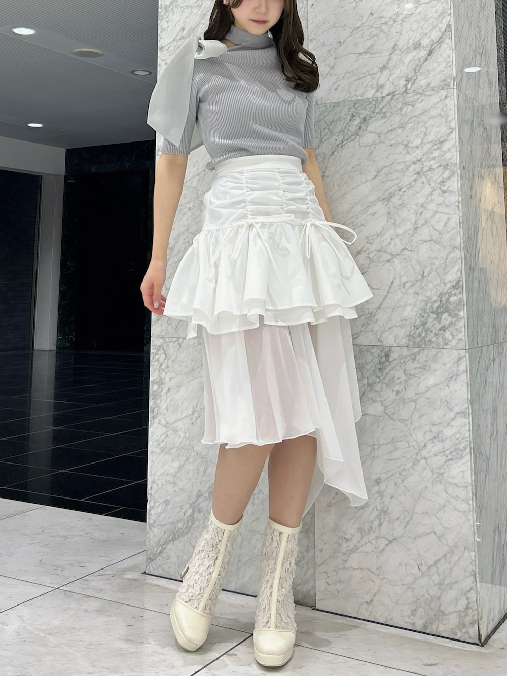 グレー系のニット/セーター、ホワイト系のスカート、ホワイト系のブーツを着用したレディースの春コーディネートの2枚目の写真