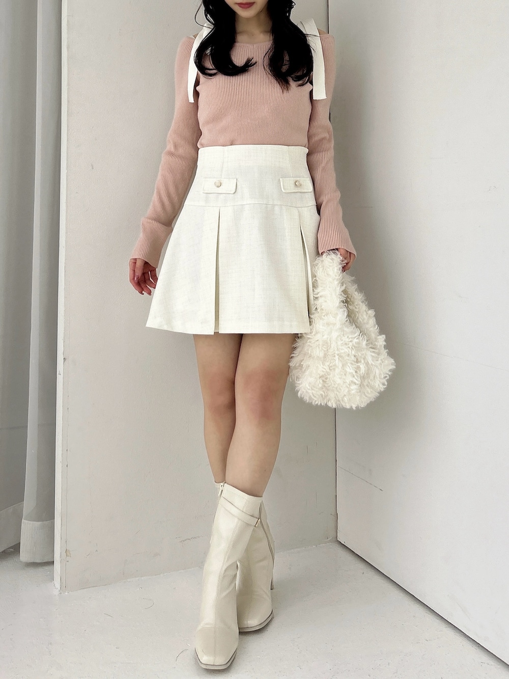 ピンク系のニット/セーター、ホワイト系のスカート、ホワイト系のブーツを着用したレディースの冬コーディネートの3枚目の写真
