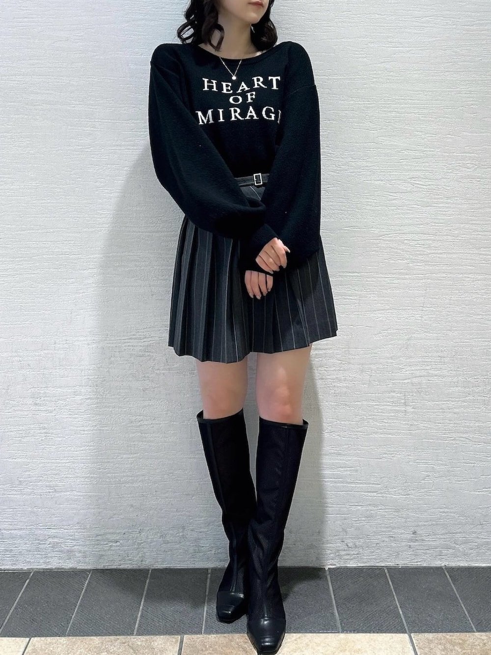 ブラック系のニット/セーター、グレー系のスカート、ブラック系のブーツを着用したレディースの春コーディネートの2枚目の写真