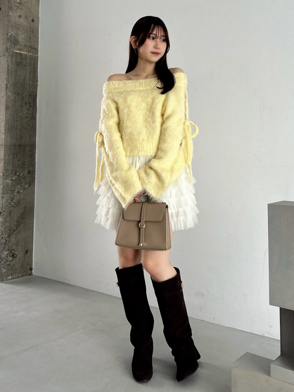 イエロー系のニット/セーター、ホワイト系のスカート、ブラウン系のブーツを着用したレディースの秋コーディネートの3枚目の写真