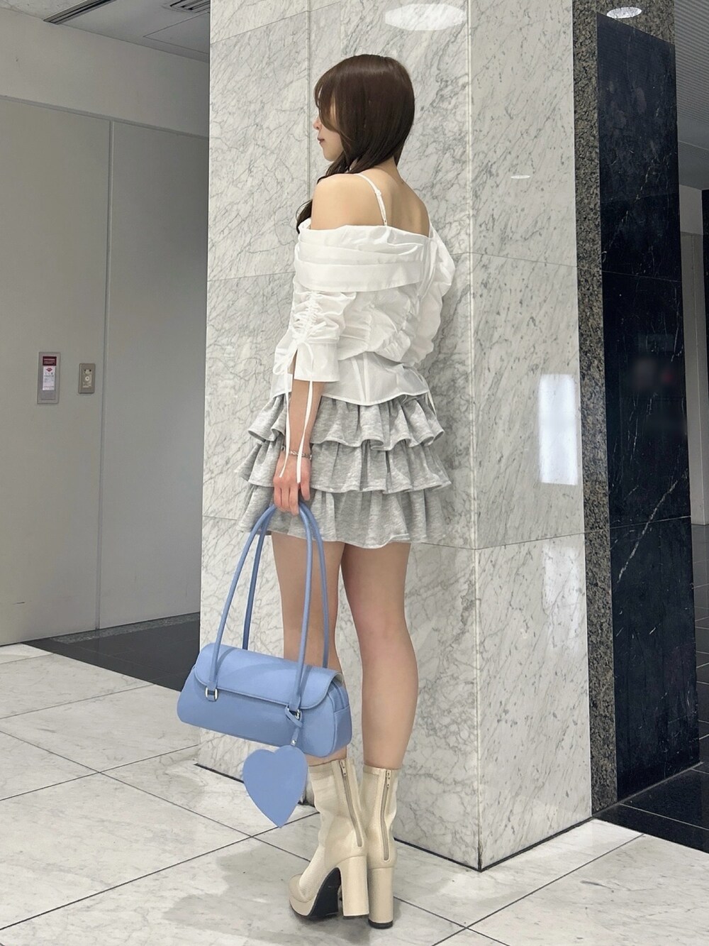 グレー系のスカート、ブルー系のハンドバッグ、ベージュ系のブーツを着用したレディースの春コーディネートの3枚目の写真