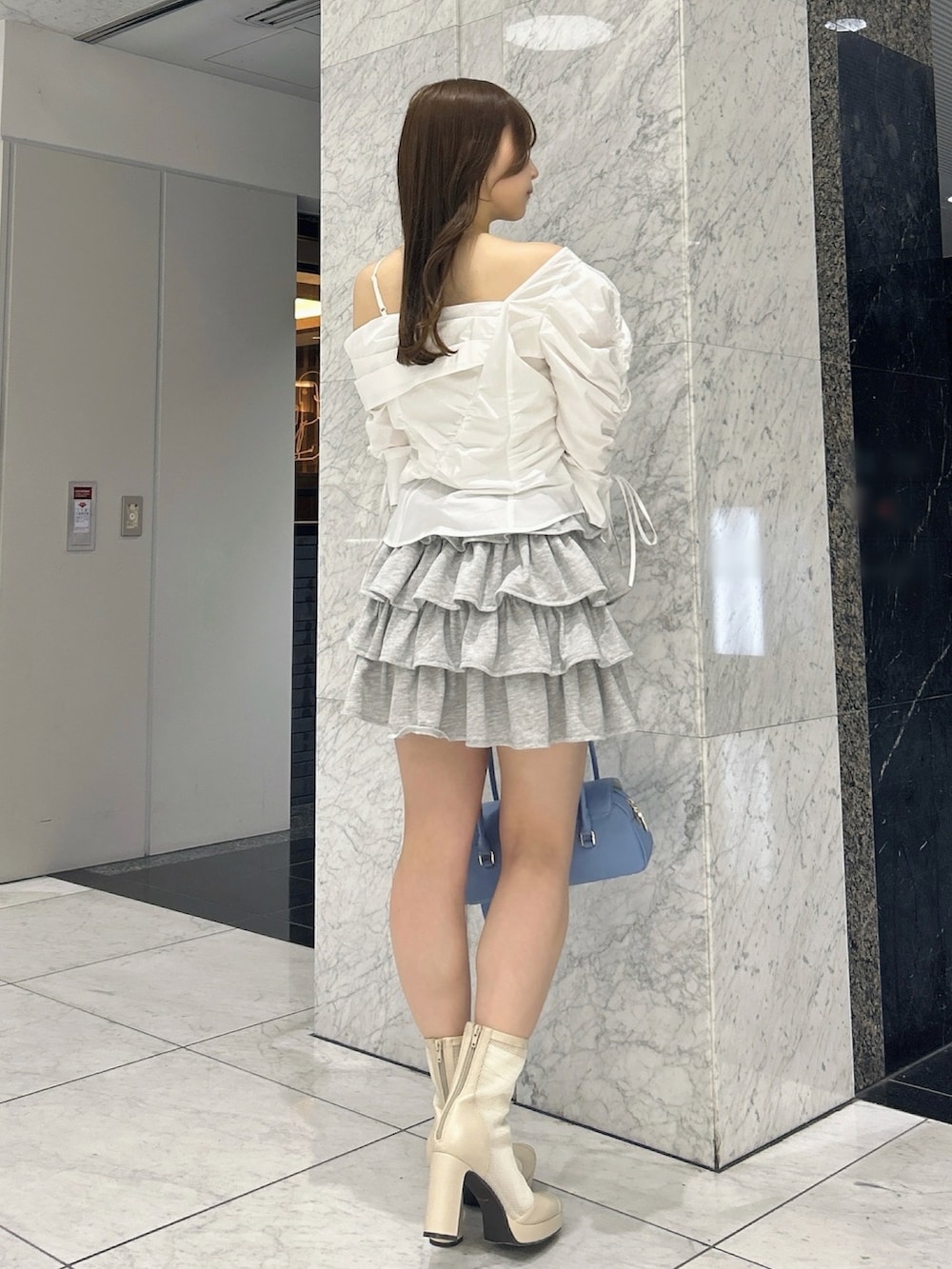 グレー系のスカート、ブルー系のハンドバッグ、ベージュ系のブーツを着用したレディースの春コーディネートの5枚目の写真