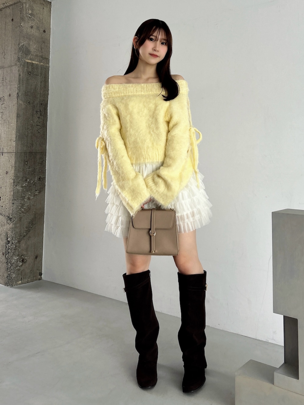 イエロー系のニット/セーター、ホワイト系のスカート、ブラウン系のブーツを着用したレディースの秋コーディネートの4枚目の写真