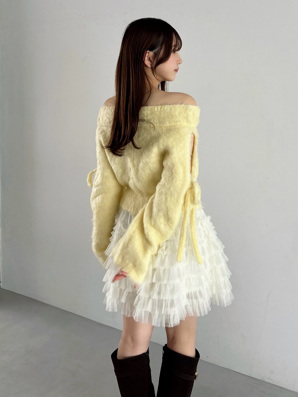 イエロー系のニット/セーター、ホワイト系のスカート、ブラウン系のブーツを着用したレディースの秋コーディネートの10枚目の写真