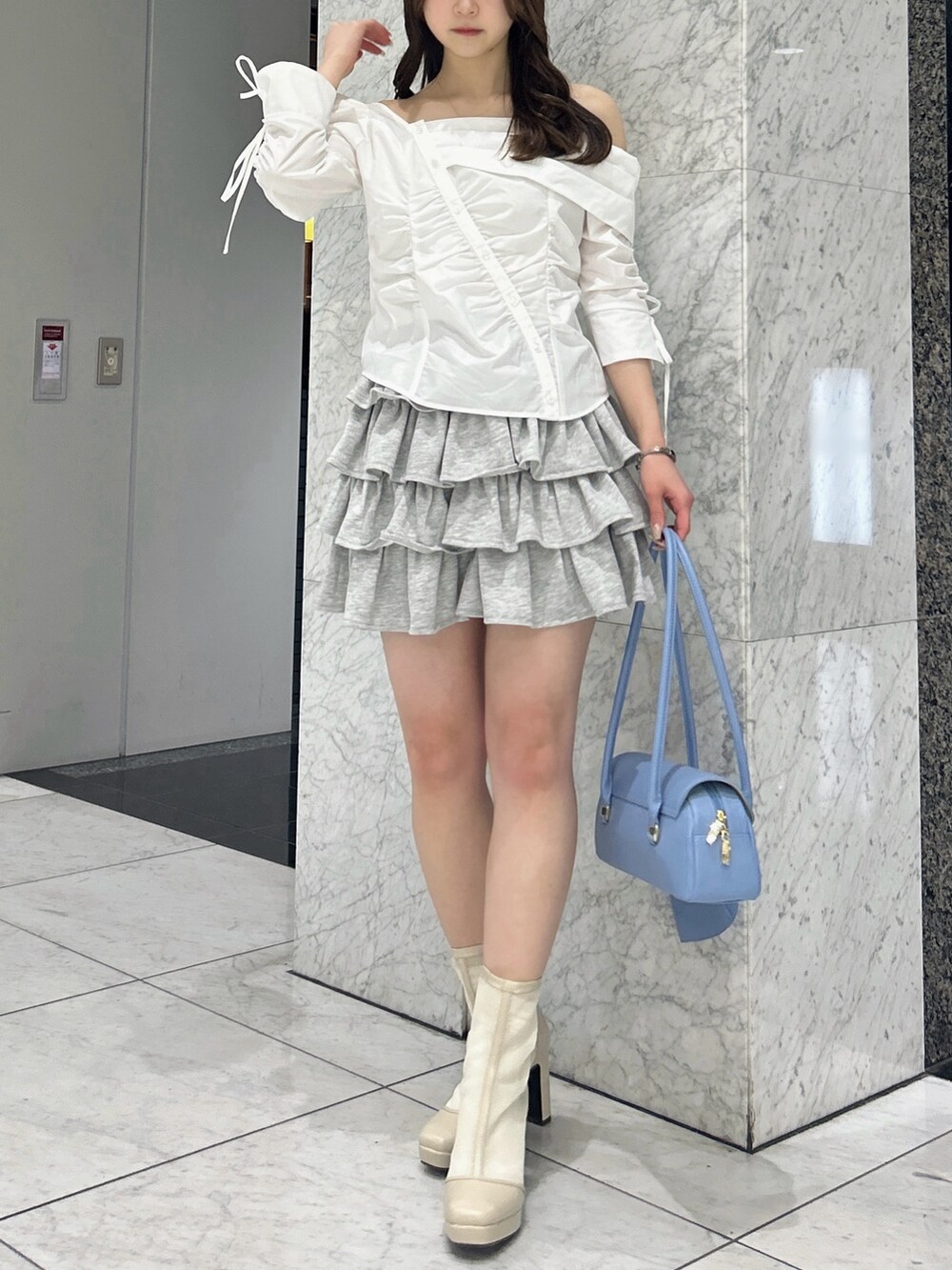 グレー系のスカート、ブルー系のハンドバッグ、ベージュ系のブーツを着用したレディースの春コーディネートの2枚目の写真