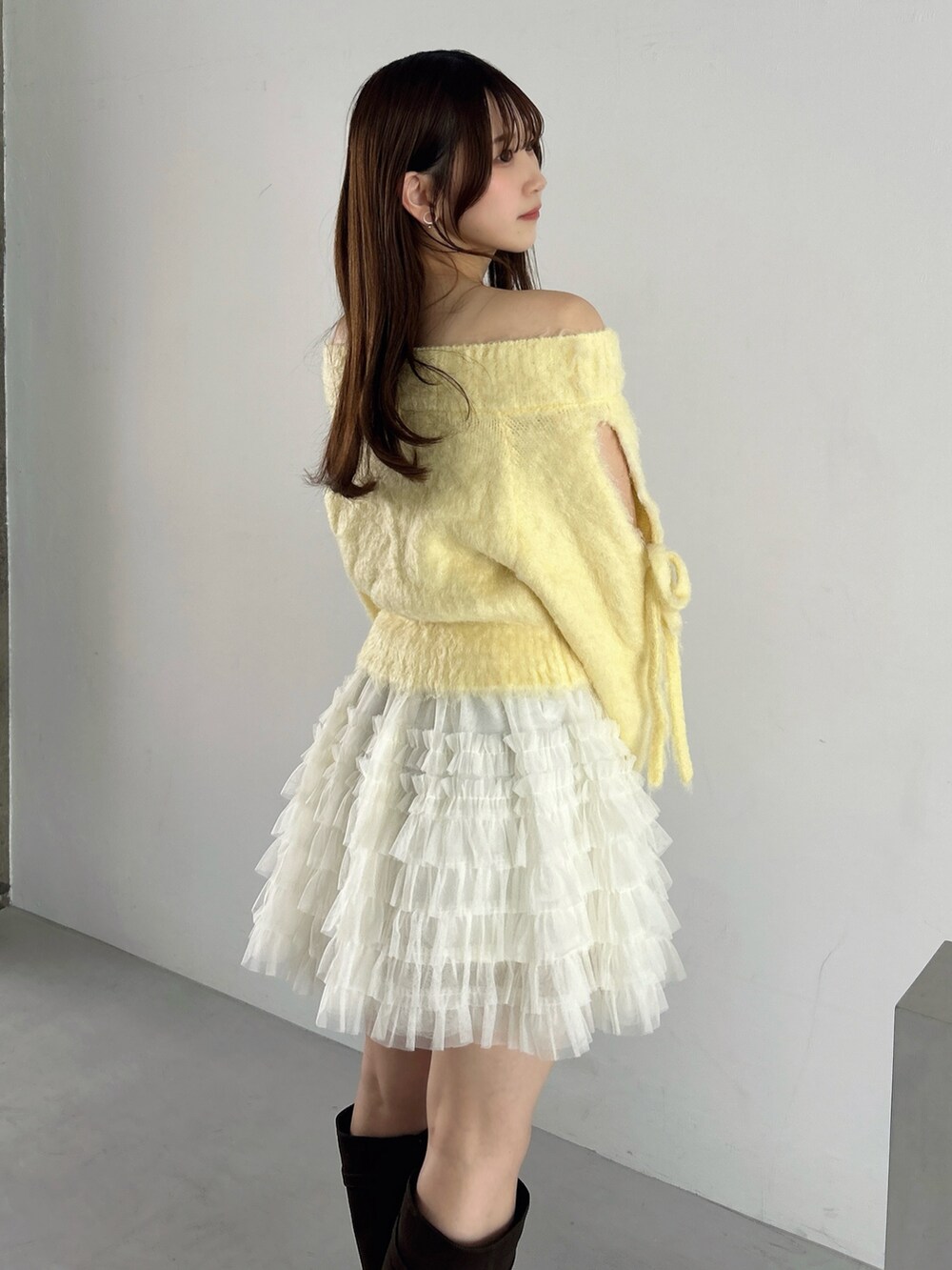 イエロー系のニット/セーター、ホワイト系のスカート、ブラウン系のブーツを着用したレディースの秋コーディネートの9枚目の写真