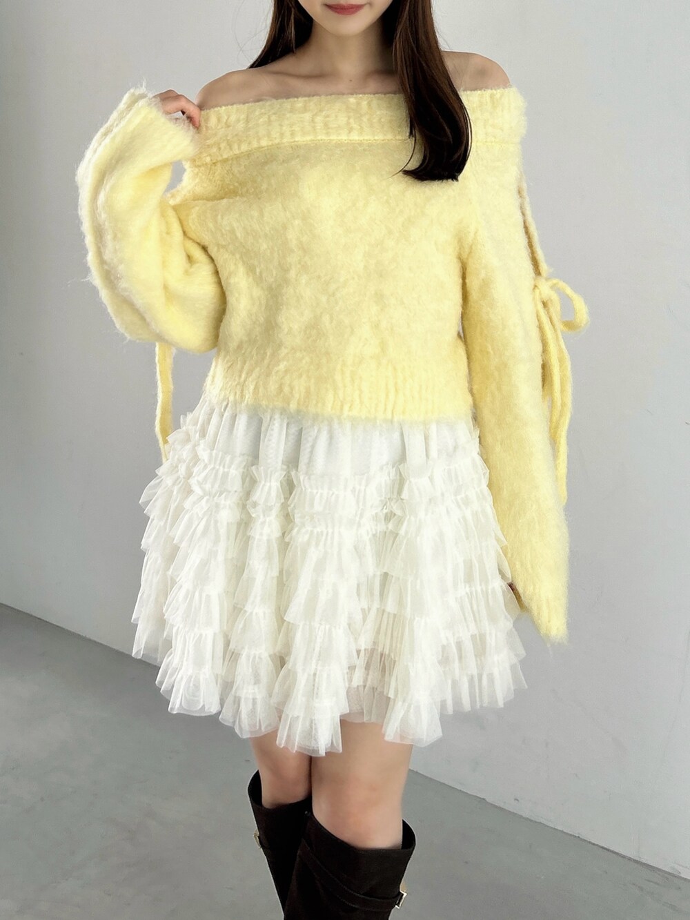 イエロー系のニット/セーター、ホワイト系のスカート、ブラウン系のブーツを着用したレディースの秋コーディネートの6枚目の写真