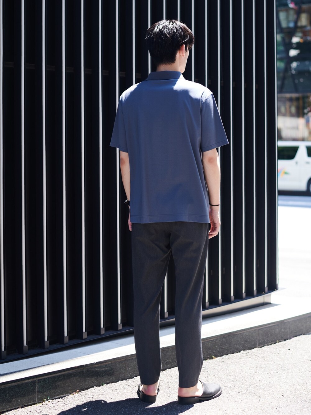 グレー系のポロシャツ、ブラック系のスラックス、ブラック系のブレスレットを着用したメンズの夏コーディネートの3枚目の写真