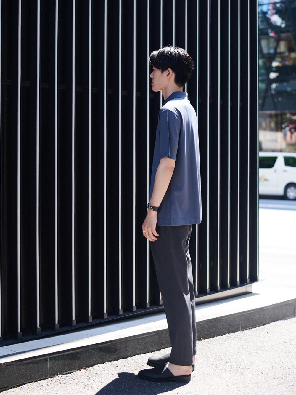 グレー系のポロシャツ、ブラック系のスラックス、ブラック系のブレスレットを着用したメンズの夏コーディネートの2枚目の写真