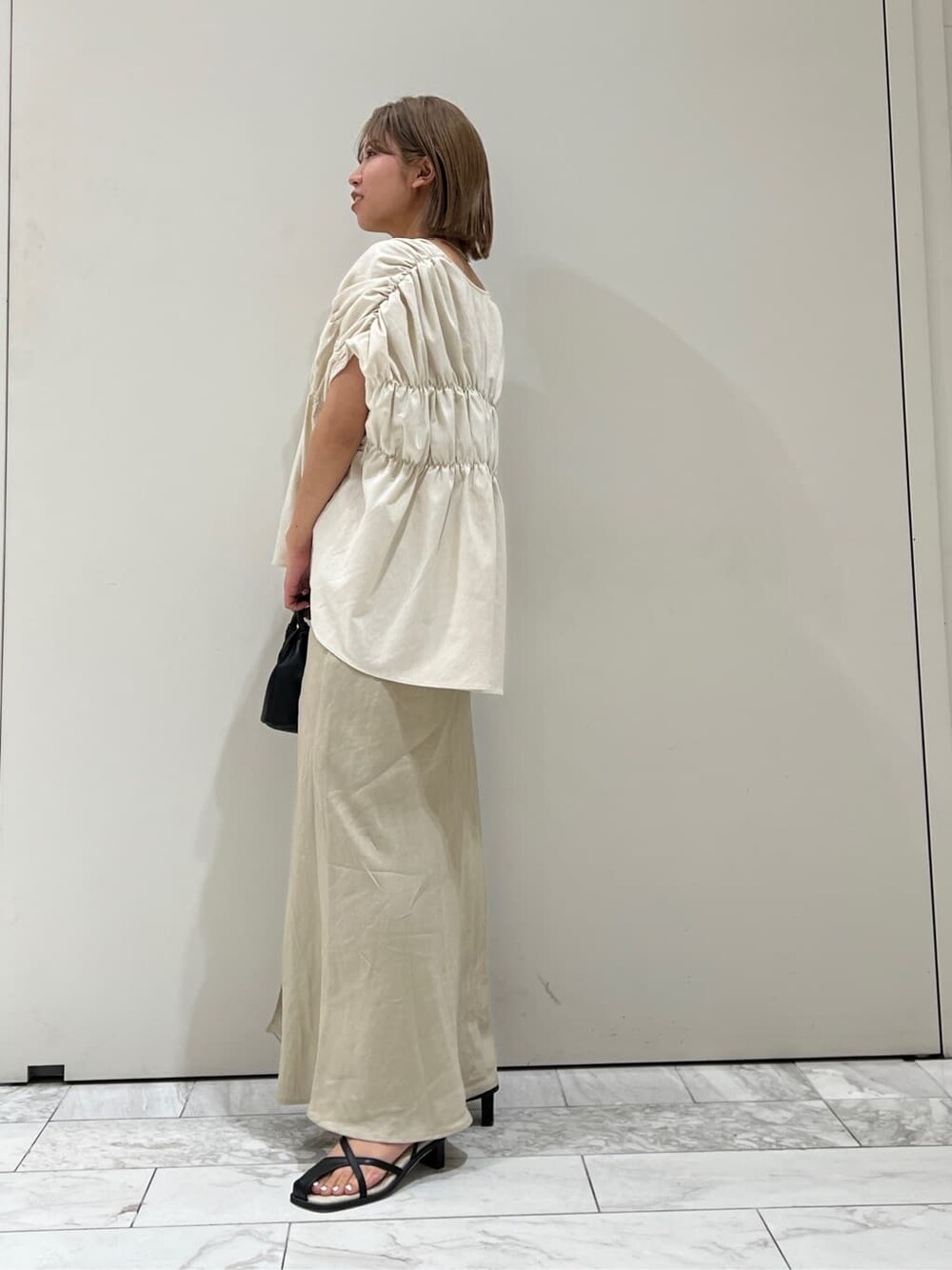 ブラック系のサンダル、ベージュ系のスカート、ホワイト系のシャツ/ブラウスを着用したレディースの夏コーディネートの6枚目の写真