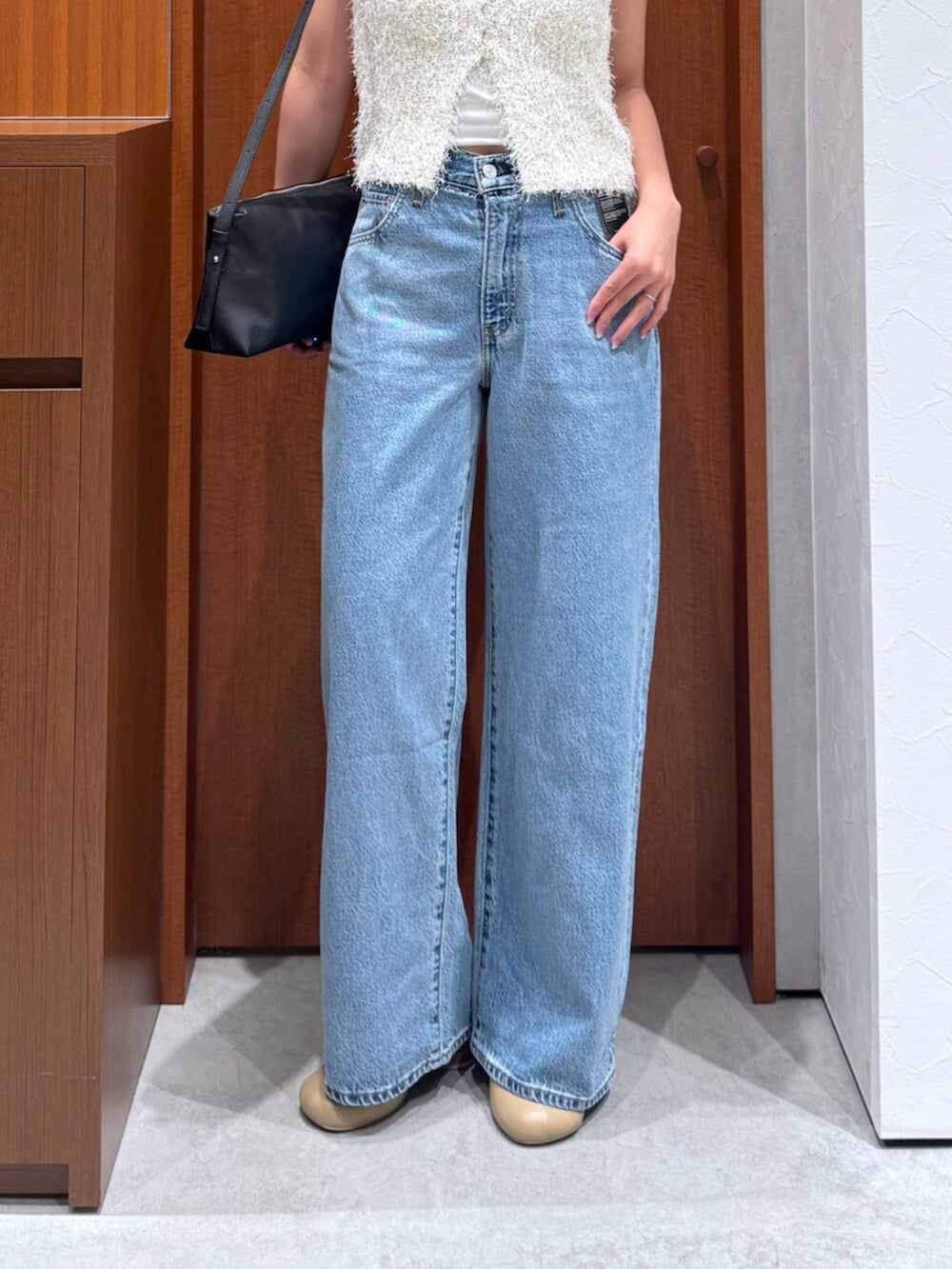 ブルー系のデニムパンツ、ホワイト系のベスト、ブラック系のハンドバッグを着用したレディースの夏コーディネートの7枚目の写真