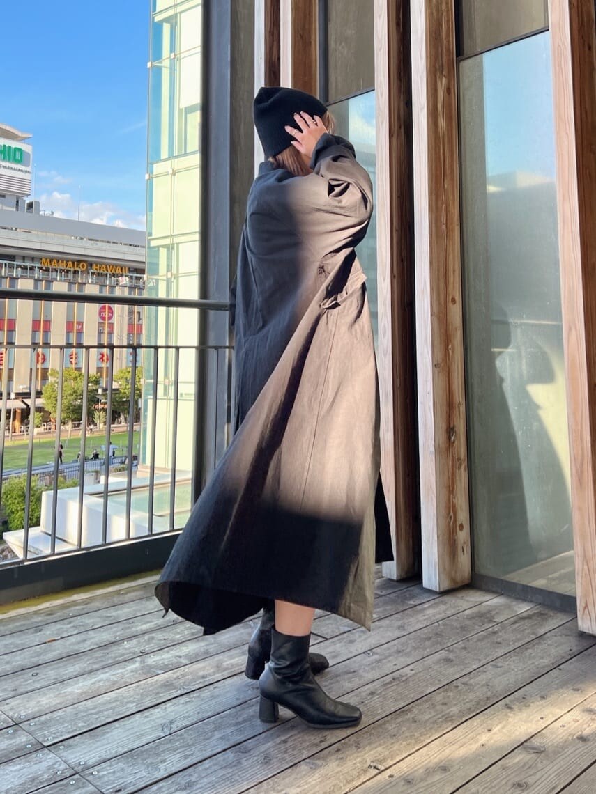 ブラック系のステンカラーコート、グリーン系のワンピース、ブラック系のブーツを着用したレディースの秋コーディネートの4枚目の写真